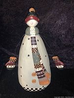 Photo of the full snowman wearing star-patterned coat, patchwork scarf, mittens on wire arms, painted face with missing carrot nose.