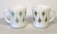 Two milk glass mugs side by side, showing diamond pattern in green and blue.