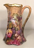 Front view of the antique porcelain hand-painted pitcher with curved handle and gold scalloped rim.