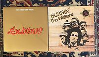 Front covers of 'Exodus' and 'Burnin'' vinyl albums by Bob Marley & The Wailers on a patterned cloth background.