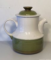 Front angle view of Denby Rochester teapot with handle on left, showing olive green lower band and cream upper portion, with lid on top.