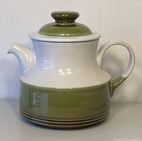 Front view of Denby Pottery Rochester small teapot, showing cream upper body and handle, olive green lower body with brown stripes, and matching lid with knob on top.