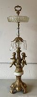 Front view showing gold gilt brass base with cherub figures, Italian marble ring, cut glass ashtray top, and hanging crystals.