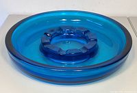 Angled front view showing the large circular blue glass ashtray with inner ring and cigarette rests.