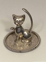 Front and side view of silver-tone metal cat ring holder sitting on round decorative base with beaded border.