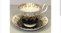 Tea cup and saucer photographed from front view showing gold floral pattern detailing on black and white background.