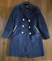 Front view of navy blue double-breasted ladies winter coat with gold buttons and gold braided trim on pockets.