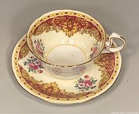 Top view of teacup placed on saucer showing maroon and gold ornate and floral design inside and outside rim of teacup and on saucer rim