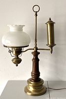 Front view of vintage brass bridge lamp with milk glass shade and brass counterweight arm on wooden and brass base.