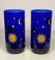 Front view of two cobalt blue glasses with gold and blue sun, moon, and star decorations.