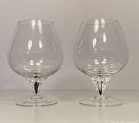 Front view showing two clear brandy snifter glasses side by side with rounded bowls and sculpted stems.