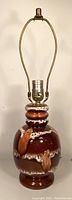 Front angle view of ceramic lamp base showing textured Fat Lava glaze in rich brown, rust and white with brass harp and push button socket.
