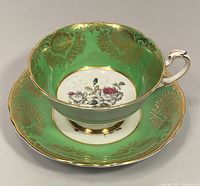 Tea cup and saucer side view showing green exterior with gold floral pattern and floral center design.
