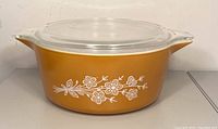 Side view of the Butterfly Gold casserole dish showing the white floral pattern on golden yellow exterior with clear glass lid on top