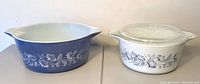 Two vintage Pyrex casserole dishes side by side, one blue and one white with lid, displaying their Colonial Mist floral pattern.