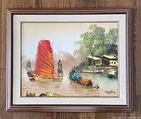 Framed oil painting showing boats on water with a red sail and riverside buildings with trees.