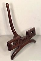 Front and side view of vintage wooden plate display stand piece showing curved vertical support and rectangular base with open geometric design, dark brown finish.