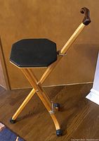 Side view of the wooden folding cane chair showing the light wood frame, black octagonal padded seat, and curved wooden handle with rubber feet on legs.