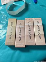 Four unopened Glowflow highlighter sticks boxed in gradient beige to rose gold packaging shown side by side