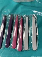 Photo showing six new, individually packaged tweezers in different colors on a blue background.