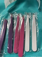 Photo of six tweezers in assorted colors, individually wrapped in plastic.