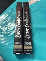 Two boxed Ardell Brow Confidential Brow Duo Taupe products displayed on a blue surface