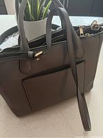 Gray purse shown from an angle highlighting the textured material, double zipper closures, and front pocket.