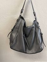 Side view of gray purse showing adjustable strap, zipper, and slouchy shape