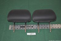 Two black leather Infiniti headrests displayed side by side on a green background with a ruler below showing measurements in inches.