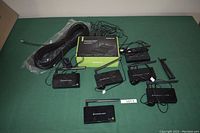 IOGEAR Wireless HDMI extender kit components including transmitter, receiver units, antennas, power adapters, and cables laid out on a green surface.