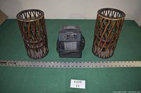 Photo shows a small portable electric heater flanked by two brown woven cylindrical candle stands on a green surface with a ruler and a lot label.