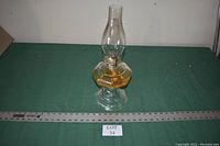 Single large vintage hurricane lantern shown on green fabric background with measuring tape for scale.