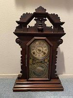 Full frontal view of the antique wooden tabletop clock showing carved decoration and octagonal glass door.