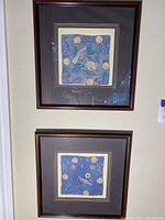Photo showing the two framed art prints mounted vertically on a wall with wooden frames and double mattes.
