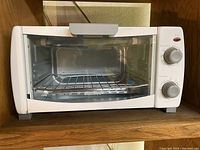 Front view of white Comfee mini toaster oven with clear glass door and two control knobs on the right side.