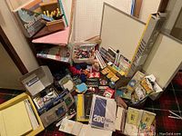 Wide view of assorted craft and school materials showing pastel board, papers, notebooks, whiteboard, crayons, markers, and various craft items.