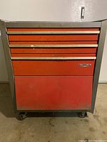 Front view of the red Craftsman rolling tool chest showing three drawers and larger fold-up door, on wheels, slightly dirty.