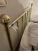 Close-up photo showing polished brass ball finial and vertical bars of the headboard with mattress partly visible.