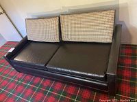 Front view of sleeper sofa showing two houndstooth patterned back cushions and black faux leather seat cushions and frame.
