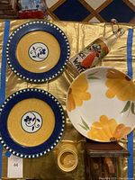 Two Mikasa Firenze plates with blue rims, yellow center and floral motif, Toscany flower bowl, vintage shoe stretcher with wooden bookend and vintage painted bottle.
