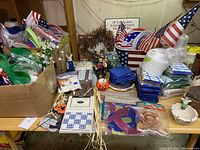 Overview of the entire lot showing party supplies, tableware, and decorations including fall scarecrow, ceramic figurines, and plastic cups with patriotic themes.