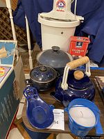 Various blue kitchen and decorative items including ceramic pot with lid, enamel teapot, small pot, spoon holder, and candle in blue pail