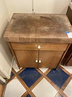 Front view of the wooden kitchen buffet showing butcher block top with heavy wear and the double door cabinet with white knobs.