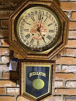 Full view of octagonal Coca Cola clock face with Roman numerals and date ring. Wooden frame with detailed carving. Clock face shows text 'Delicious Drink Coca Cola 5 Refreshing'. Clock hands visible indicating time. Lower glass door reveals brass pendulum and 'REGULATOR' text.