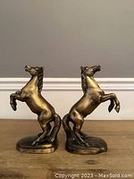 Full frontal photo of both brass/bronze horse figurines side by side on a wooden surface.