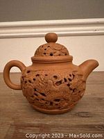 Front side of the teapot showing round form, lid with knob, handle and spout, featuring openwork carvings of mythical beasts and foliage.