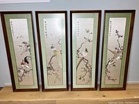 Four framed embroidered silk panels side by side against wall