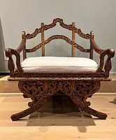 Full front view of carved wooden howdah replica with white cushion on hardwood floor