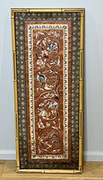 Full vertical view of embroidered fabric artwork framed in bamboo-style frame against a light wall.