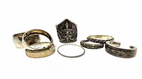 Seven silver bracelets arranged: plain cuff, two hinged bangles, thin wire band, ornate dancer cuff, three open motif cuffs